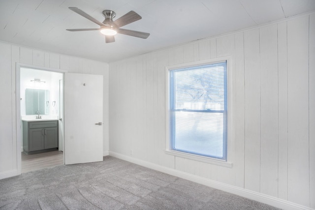 unfurnished bedroom featuring sink, wooden walls, ceiling fan, connected bathroom, and light colored carpet