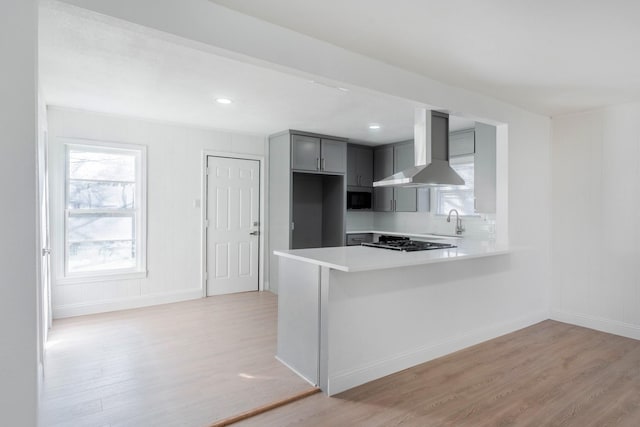 kitchen with sink, wall chimney range hood, kitchen peninsula, light hardwood / wood-style floors, and gray cabinets