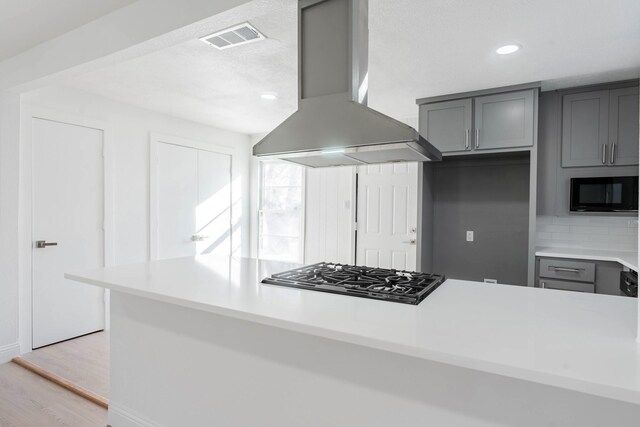 kitchen with decorative backsplash, gray cabinets, wall chimney range hood, and stainless steel gas cooktop