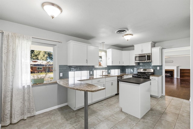 kitchen featuring tasteful backsplash, appliances with stainless steel finishes, kitchen peninsula, pendant lighting, and white cabinets