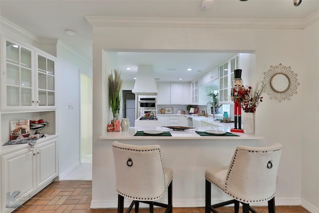 kitchen featuring white cabinets, a kitchen breakfast bar, kitchen peninsula, and crown molding