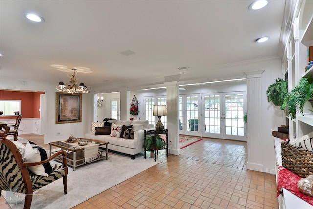 living room featuring ornate columns, crown molding, french doors, and a notable chandelier