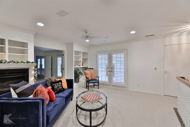 living room with built in shelves, ceiling fan, french doors, crown molding, and light carpet