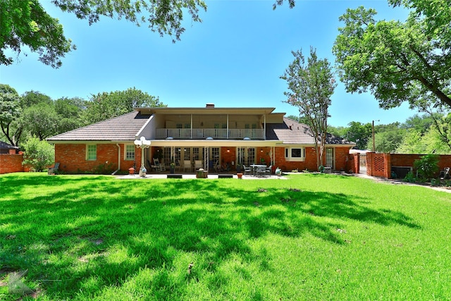 rear view of property with a yard, a balcony, and a patio