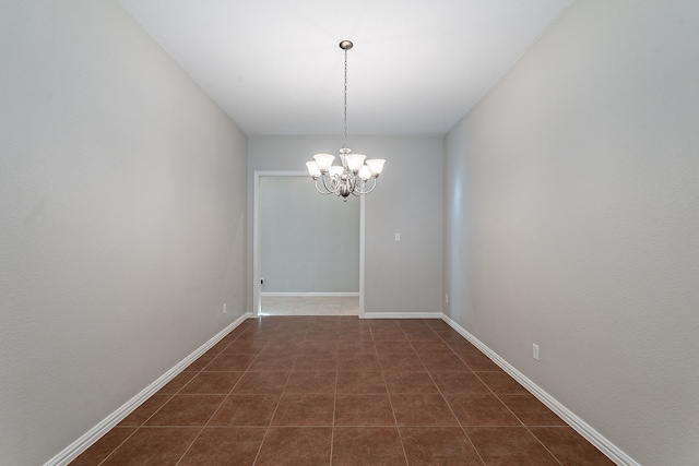 spare room with dark tile patterned flooring and an inviting chandelier