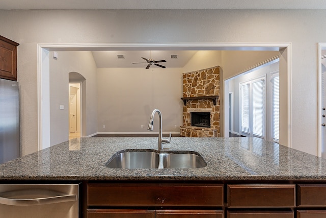 kitchen featuring a fireplace, ceiling fan, sink, stone counters, and stainless steel refrigerator