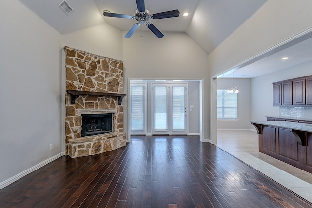 living room featuring dark hardwood / wood-style floors, a stone fireplace, lofted ceiling, and ceiling fan with notable chandelier