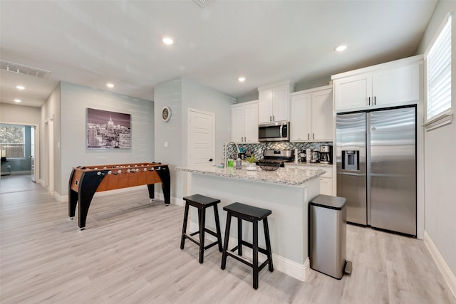 kitchen with a kitchen island with sink, white cabinets, light hardwood / wood-style flooring, light stone countertops, and stainless steel appliances