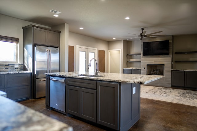 kitchen featuring appliances with stainless steel finishes, light stone counters, a kitchen island with sink, sink, and gray cabinets