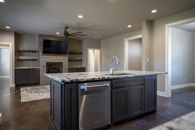 kitchen featuring sink, ceiling fan, light stone countertops, a fireplace, and an island with sink