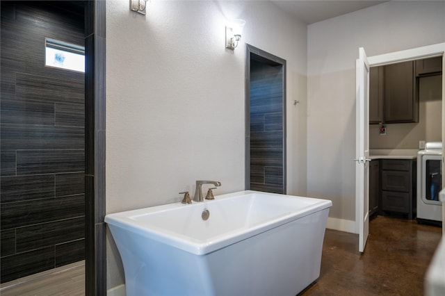 bathroom with washer / dryer, concrete flooring, and a tub to relax in