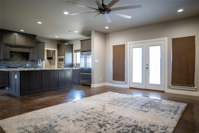 kitchen with a center island with sink, light stone counters, gray cabinetry, and appliances with stainless steel finishes