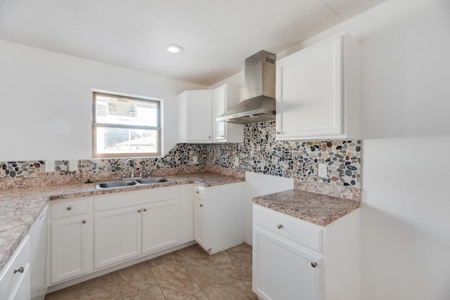 kitchen with backsplash, white cabinets, sink, and wall chimney range hood