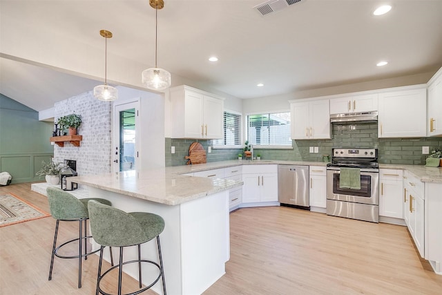 kitchen featuring kitchen peninsula, a breakfast bar, stainless steel appliances, and white cabinetry