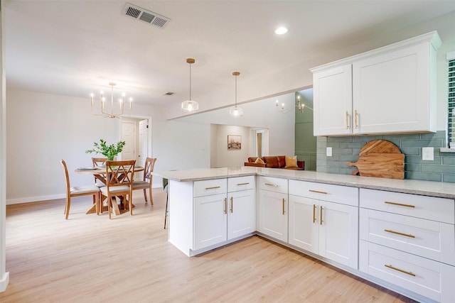 kitchen featuring tasteful backsplash, kitchen peninsula, light hardwood / wood-style floors, decorative light fixtures, and white cabinets