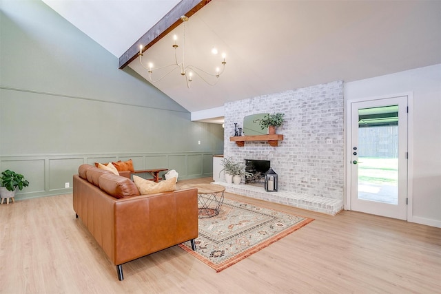 living room with a brick fireplace, an inviting chandelier, light hardwood / wood-style flooring, and vaulted ceiling