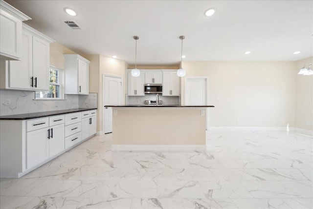 kitchen featuring white cabinets, backsplash, decorative light fixtures, and an island with sink