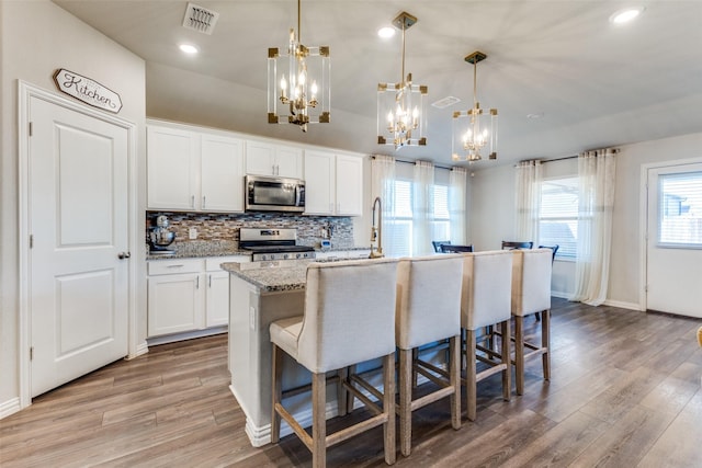 kitchen featuring a kitchen bar, appliances with stainless steel finishes, a kitchen island with sink, pendant lighting, and white cabinetry