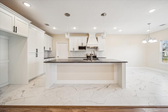 kitchen with hanging light fixtures, sink, white cabinets, and premium range hood