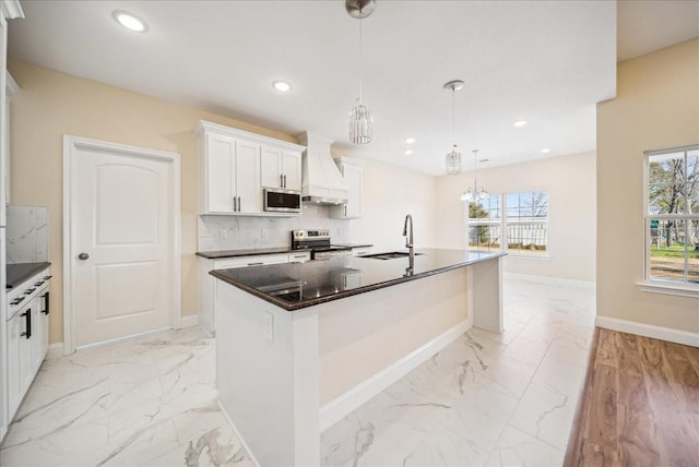 kitchen featuring custom exhaust hood, a kitchen island with sink, sink, appliances with stainless steel finishes, and white cabinetry