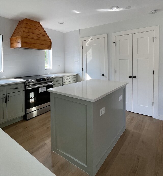 kitchen with tasteful backsplash, stainless steel range with electric stovetop, a center island, light hardwood / wood-style flooring, and custom range hood