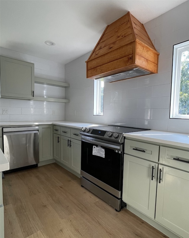 kitchen featuring decorative backsplash, appliances with stainless steel finishes, light hardwood / wood-style floors, and custom range hood