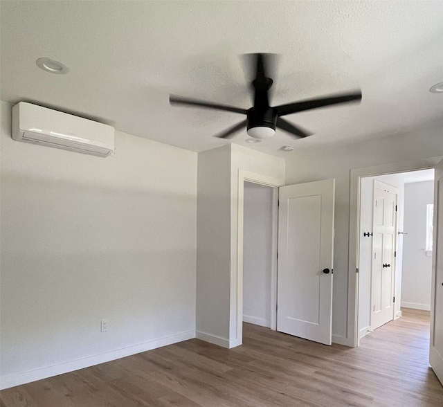 unfurnished bedroom featuring ceiling fan, wood-type flooring, a textured ceiling, and an AC wall unit