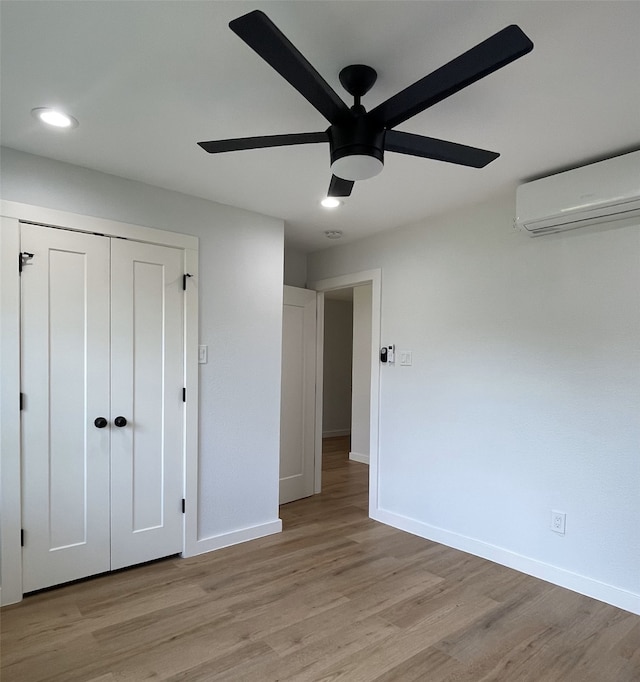 unfurnished bedroom with ceiling fan, light wood-type flooring, a closet, and an AC wall unit