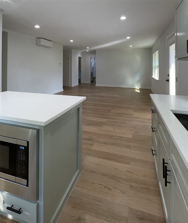 kitchen featuring stainless steel microwave, a center island, light hardwood / wood-style flooring, and an AC wall unit