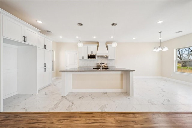 kitchen featuring stainless steel microwave, white cabinets, pendant lighting, and custom exhaust hood