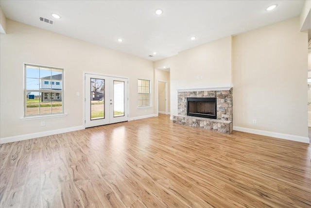 unfurnished living room with a healthy amount of sunlight, light wood-type flooring, a fireplace, and french doors