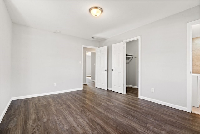 unfurnished bedroom featuring a walk in closet, a closet, and dark wood-type flooring