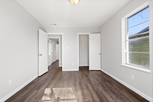 unfurnished bedroom with a spacious closet, dark wood-type flooring, and a closet