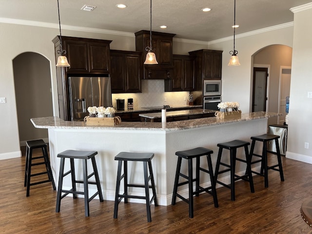 kitchen featuring stainless steel appliances, backsplash, a large island with sink, decorative light fixtures, and a kitchen bar