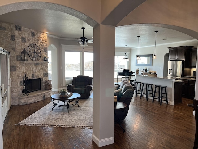 living room with dark hardwood / wood-style flooring, a stone fireplace, ceiling fan, and ornamental molding