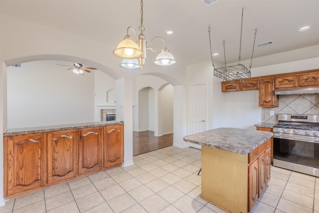 kitchen featuring tasteful backsplash, ceiling fan with notable chandelier, decorative light fixtures, stainless steel range oven, and a kitchen island