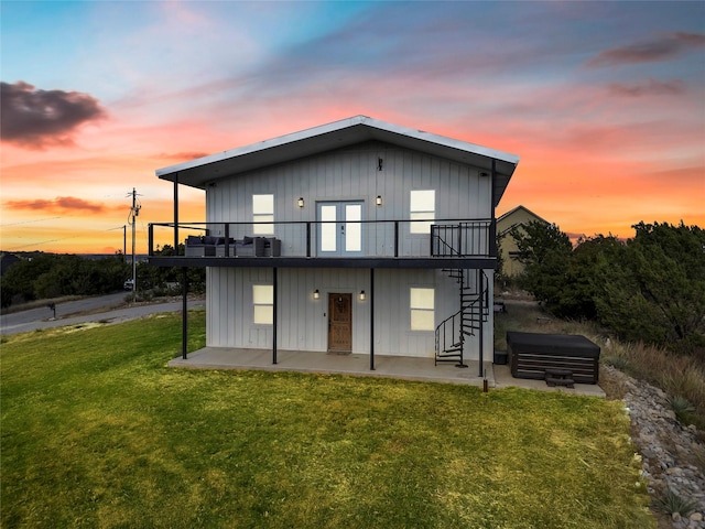 back house at dusk with a patio area and a lawn