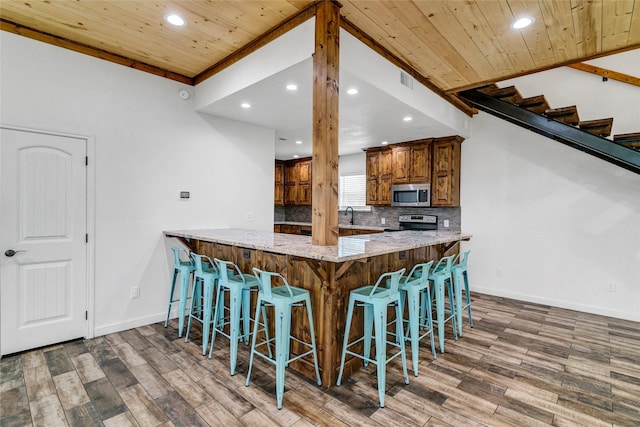 kitchen featuring stainless steel appliances, light stone counters, kitchen peninsula, a breakfast bar, and ornamental molding