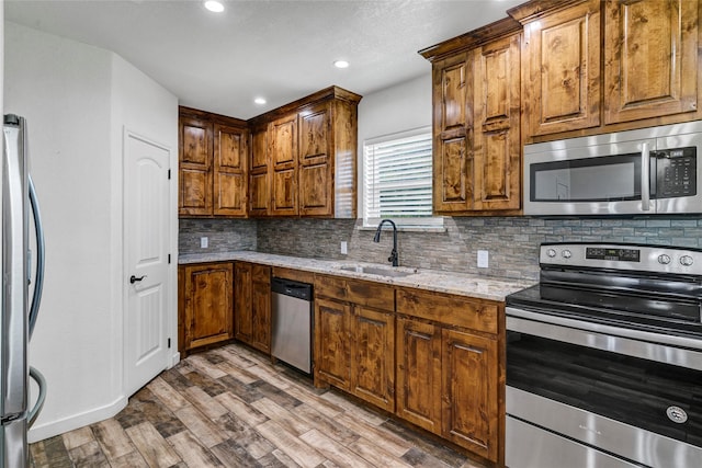 kitchen with light stone countertops, appliances with stainless steel finishes, tasteful backsplash, sink, and hardwood / wood-style flooring