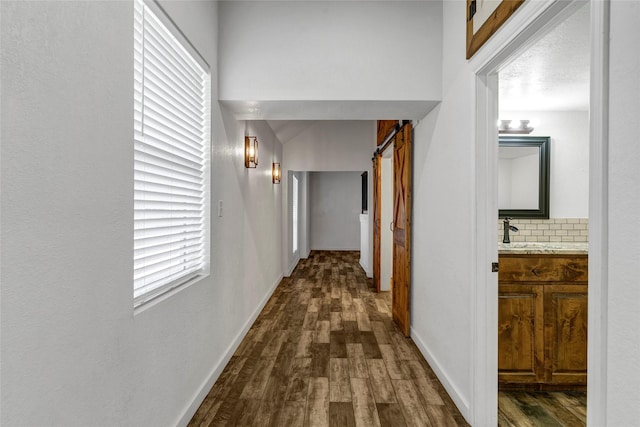 corridor with a barn door, sink, dark wood-type flooring, and a textured ceiling