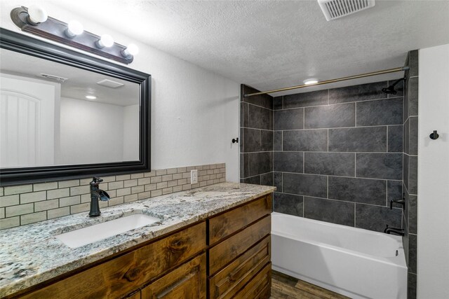 bathroom with a textured ceiling, backsplash, tiled shower / bath combo, and hardwood / wood-style floors