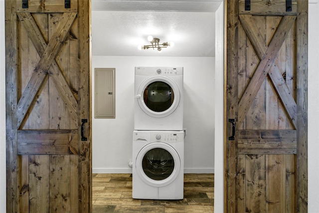 laundry room with a barn door, stacked washer and dryer, and electric panel