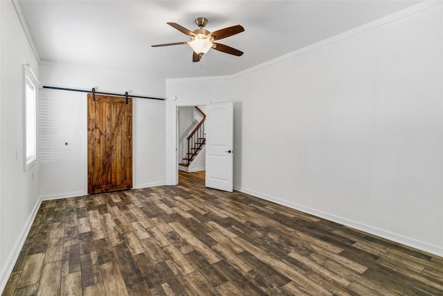 unfurnished bedroom featuring ceiling fan, a barn door, ornamental molding, and dark wood-type flooring