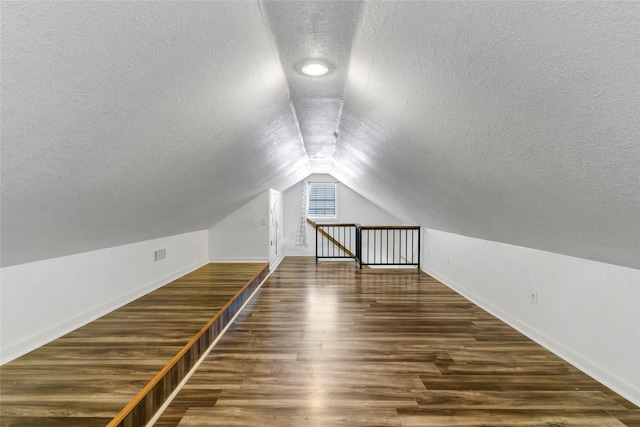 additional living space featuring lofted ceiling, a textured ceiling, and dark wood-type flooring