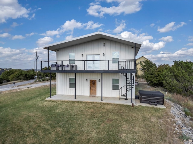 rear view of property with a hot tub, a patio, and a yard