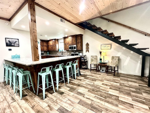 kitchen featuring stainless steel appliances, light hardwood / wood-style flooring, kitchen peninsula, decorative backsplash, and a breakfast bar