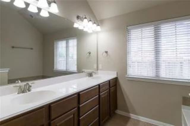 bathroom with vaulted ceiling, vanity, and a bathtub