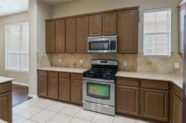 kitchen with appliances with stainless steel finishes, light tile patterned floors, and decorative backsplash