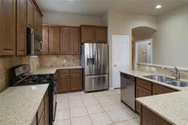 kitchen with light tile patterned flooring, appliances with stainless steel finishes, sink, decorative backsplash, and light stone countertops