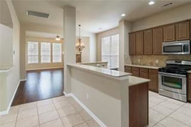 kitchen with backsplash, stainless steel appliances, hanging light fixtures, and light tile patterned flooring